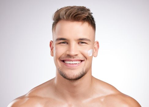 Studio shot of a young man applying moisturizer to his face against a grey background.
