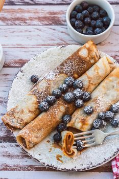 Dish with delicious homemade pancakes or crepes filled with dulce de leche. Fork with a bite and some spiked blueberries.vertical orientation