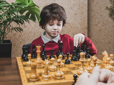 School age Boy playing chess indoors, making decision on the next move. Leisure activities for kids