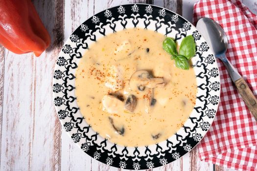 A Homemade cream of chicken and mushroom soup or French style chicken fricassee, in a soup bowl on a wooden table. Aerial view