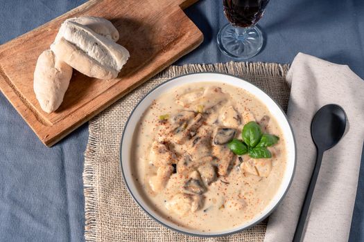 A Homemade cream of chicken and mushroom soup or French style chicken fricassee, in a soup bowl on a wooden table. Aerial view