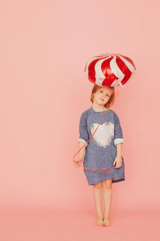 Portrait of an excited pretty little girl celebrating birthday and holding balloon in hand on over pink background