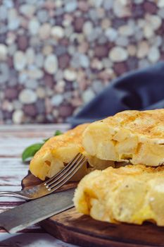 high view of a plate with a Spanish potato omelette cut in eighths on a wooden table. VErtical orientation. Traditional food.