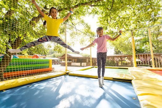 Two little girls in the summer jump on a trampoline, smiling and laughing. Children play. Relax in the fresh air. Friends jump on a trampoline. Happy child.