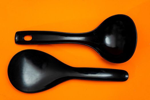 Set of kitchen spoon and spatula in black plastic isolated on orange background.