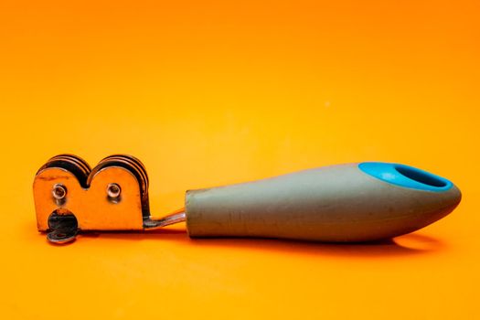 Knife sharpener isolated on an orange background. Inexpensive non-professional kitchen utensil.