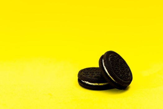 Two chocolate sandwich cookies with sweet cream on a yellow surface. Copy space.