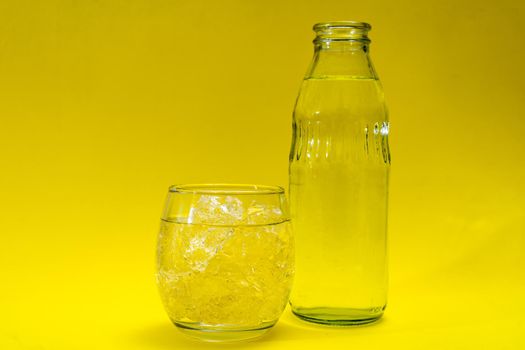 Glass beaker and bottle filled with ice and purified water. Yellow background.