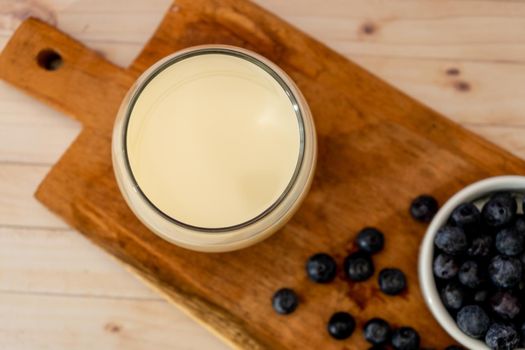 Top view of a glass of milk next to some organic blueberries on a wooden board on a table. Healthy eating