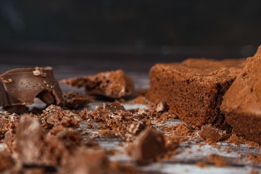 Close up of a Chocolate brownies on a rustic wooden table with chocolate chips and chocolate soil next to the brownie portions.