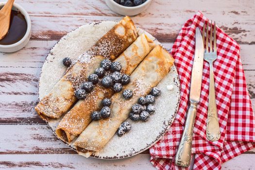 Delicious plate with homemade pancakes or crepes filled with dulce de leche and blueberries and icing sugar covering the plate. Top view