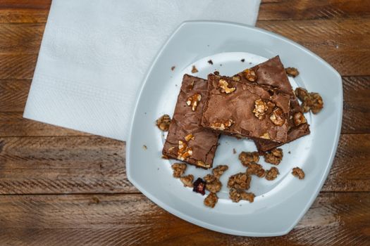 Homemade chocolate brownie squares with pecan pieces served on a white plate. Natural, healthy food concept. Top view.