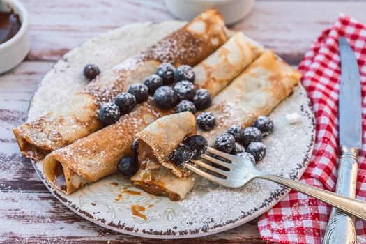 Dish with delicious homemade pancakes or crepes filled with dulce de leche. Fork with a bite and some spiked blueberries.