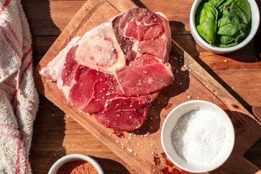 A fresh raw beef ossobuco steak on a board with garnishes on a wooden table. Animal protein concept, Italian food. Aereal view