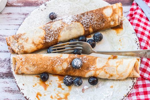 Delicious plate with homemade pancakes or crepes filled with dulce de leche and blueberries and icing sugar covering the plate. close up.