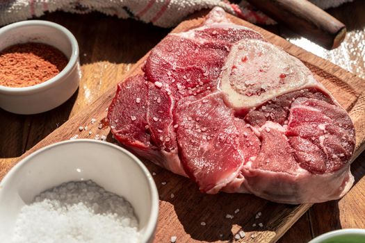 A fresh raw beef ossobuco steak on a board with garnishes on a wooden table. Animal protein concept, Italian food. Aereal view