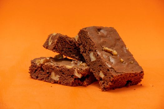 Homemade chocolate brownie squares with pecan pieces. Orange Background. Natural, healthy food concept. High view.