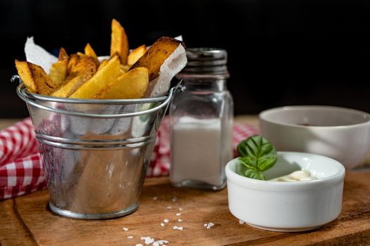 French fries in a metal pot with aioli and ketchup on a wooden board. copy space