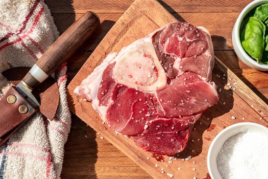 A fresh raw beef ossobuco steak on a board with garnishes on a wooden table. Animal protein concept, Italian food. Aereal view