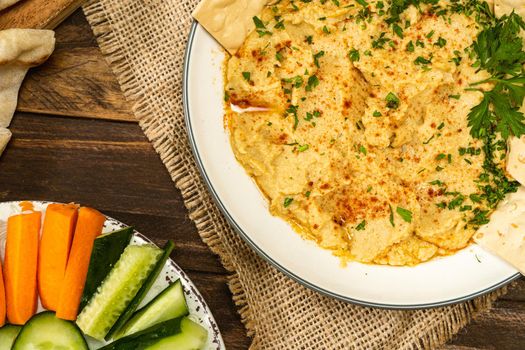 View of a bowl with homemade Hummus with crackers and in another bowl carrots and other vegetables. Fresh, healthy and natural food concept. Copy space.