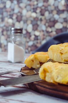 high view of a plate with a Spanish potato omelette cut in eighths on a wooden table. VErtical orientation. Traditional food.