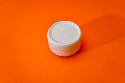 Small white plastic cream jar with lid isolated on orange background. copy space.