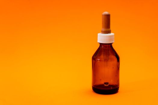Small bottle with amber glass dropper insulated on orange background. copy space.