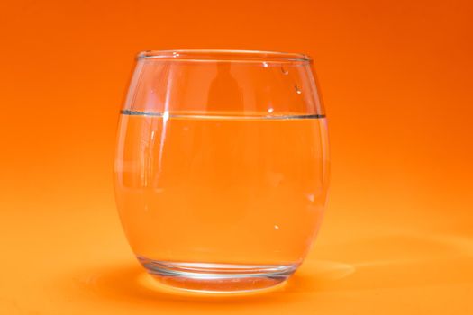 Glass tumbler with purified water on orange and light orange gradient background. Copy space