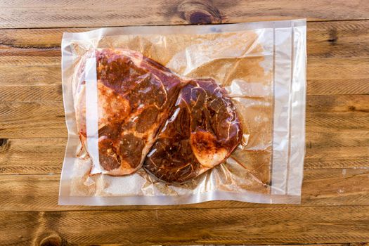 Two pieces of vacuum packed raw beef ossobuco ready for storage or sous vide cooking. Animal protein concept, avant-garde cuisine. Aereal view, Wooden background.