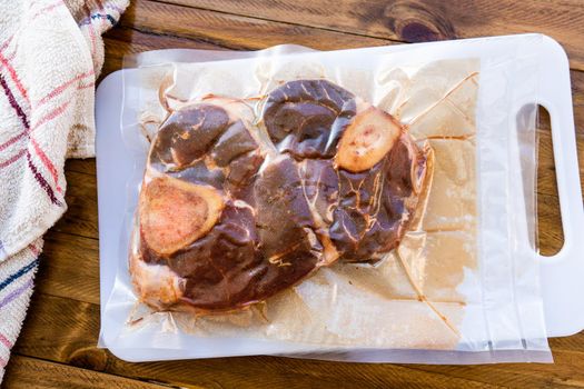 Two pieces of vacuum packed raw beef ossobuco ready for storage or sous vide cooking. Animal protein concept, avant-garde cuisine. Aereal view, Wooden background.