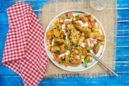 A delicious potato, chickpea, tomato and mushroom salad with parsley and aioli in a bowl on a Rustic table. Healthy, homemade, vegan food. Top view. copy space