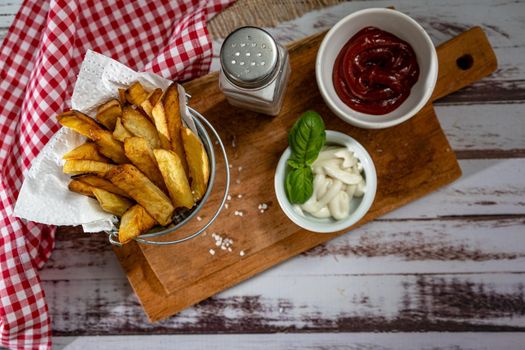 French fries in a metal pot with aioli and ketchup on a wooden board. Top view. Copy space.