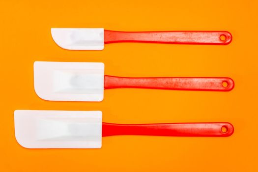 Set of three red and white kitchen spatulas made of silicone and plastic insulated on an orange surface. Kitchen and pastry utensil.