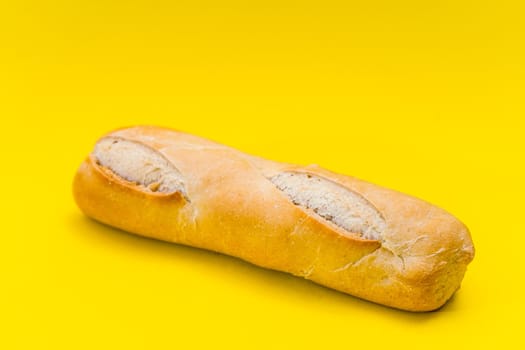Small baguete of french bakery bread on a pure yellow surface. Copy space.
