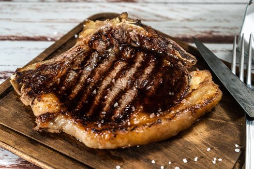 Incredible t-bone cooked on the grill or barbecue on a wooden board with cutlery on the side. High view.