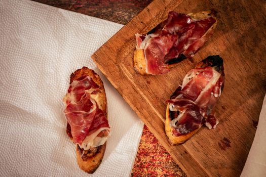 Classic Spanish tapa or brusqueta of Serrano ham with philadelphia cheese on a slice of toasted bread. Mediterranean food concept. Top view.