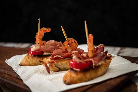 Bruschettas with serrano ham, cherry tomato and a grilled shrimp on a wooden board. Mediterranean food concept.