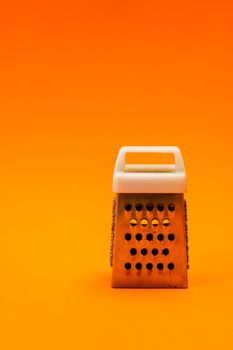 A small shiny metal grater isolated on orange background, close-up of cheese and food stainless grater.