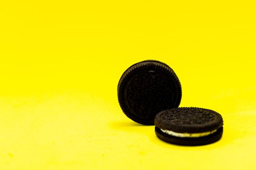 Two chocolate sandwich cookies with sweet cream on a yellow surface. Copy space.