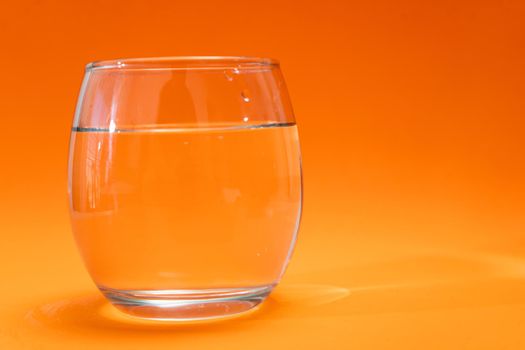 Glass tumbler with purified water on orange and light orange gradient background. Copy space