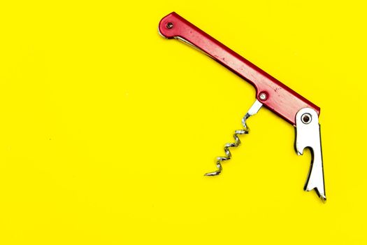 Red corkscrew or metal bottle opener on a yellow surface. Copy space.