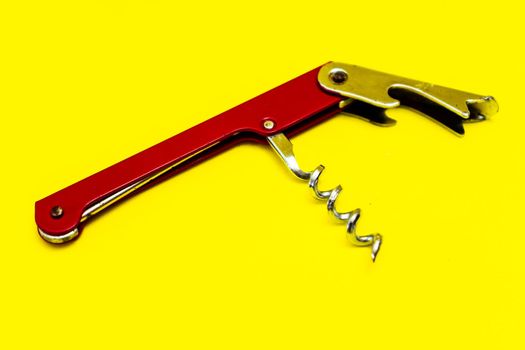 Red corkscrew or metal bottle opener on a yellow surface. Copy space.