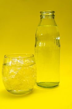 Glass beaker and bottle filled with ice and purified water. Yellow background.