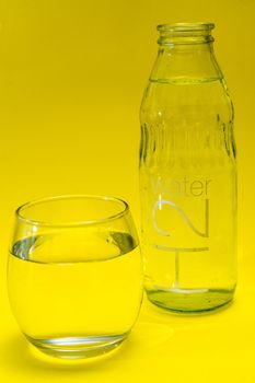 Glass beaker and bottle filled with purified water. Yelloew background.