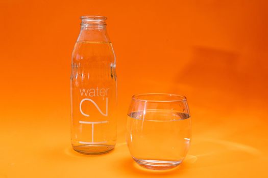 Bottle and glass tumbler with purified water in orange and light orange gradient background. Ecology concept, environment care. water care.