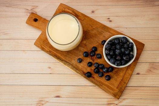 Top view of a glass of milk next to some organic blueberries on a wooden board on a table. Healthy eating