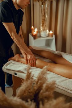 Concentrated male therapist doing professional leg massage for female client at spa center.
