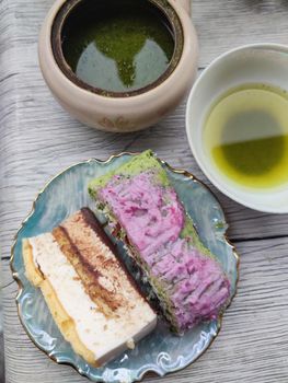 sweet fruit roll and a piece of cake on a plate, green tea in a teapot and cup, top view.