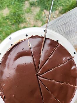 cutting round creamy chocolate cheesecake into pieces close-up