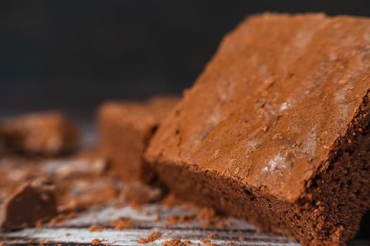 Close up of a Chocolate brownies on a rustic wooden table with chocolate chips and chocolate soil next to the brownie portions.